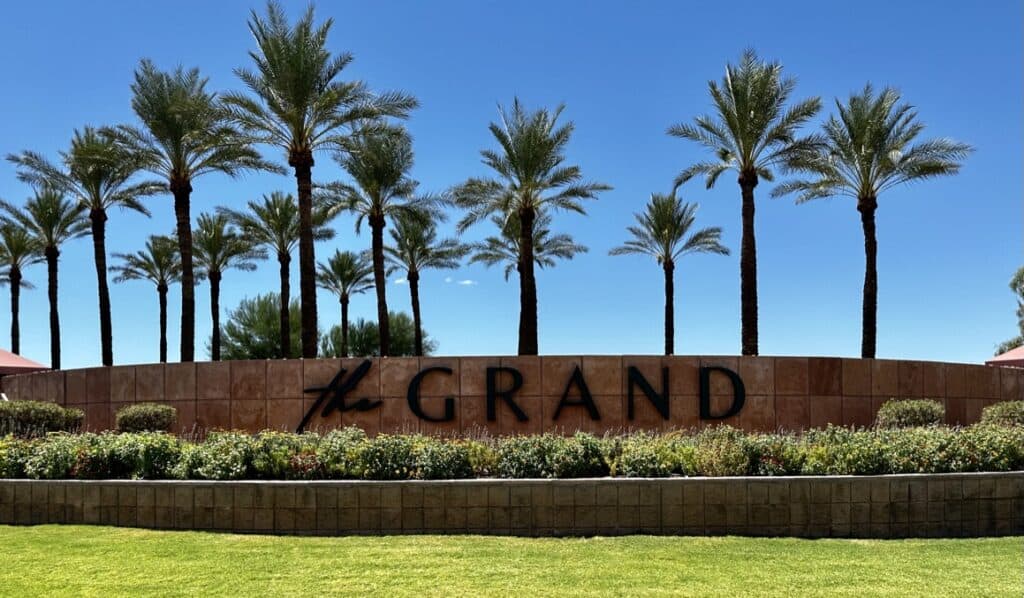 The Grand at Sun City Grand entrance — stone monument with The Grand lettering, framed by towering palm trees