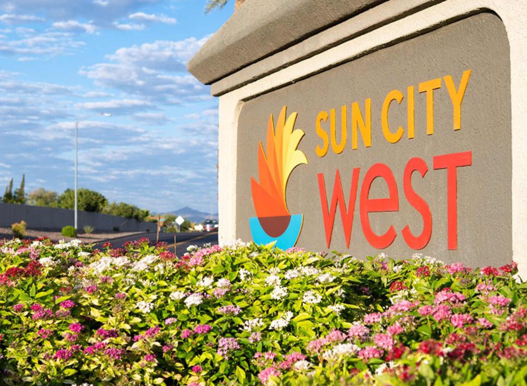 Sun City West, Arizona main entrance sign with iconic sun logo, flowering pentas in foreground